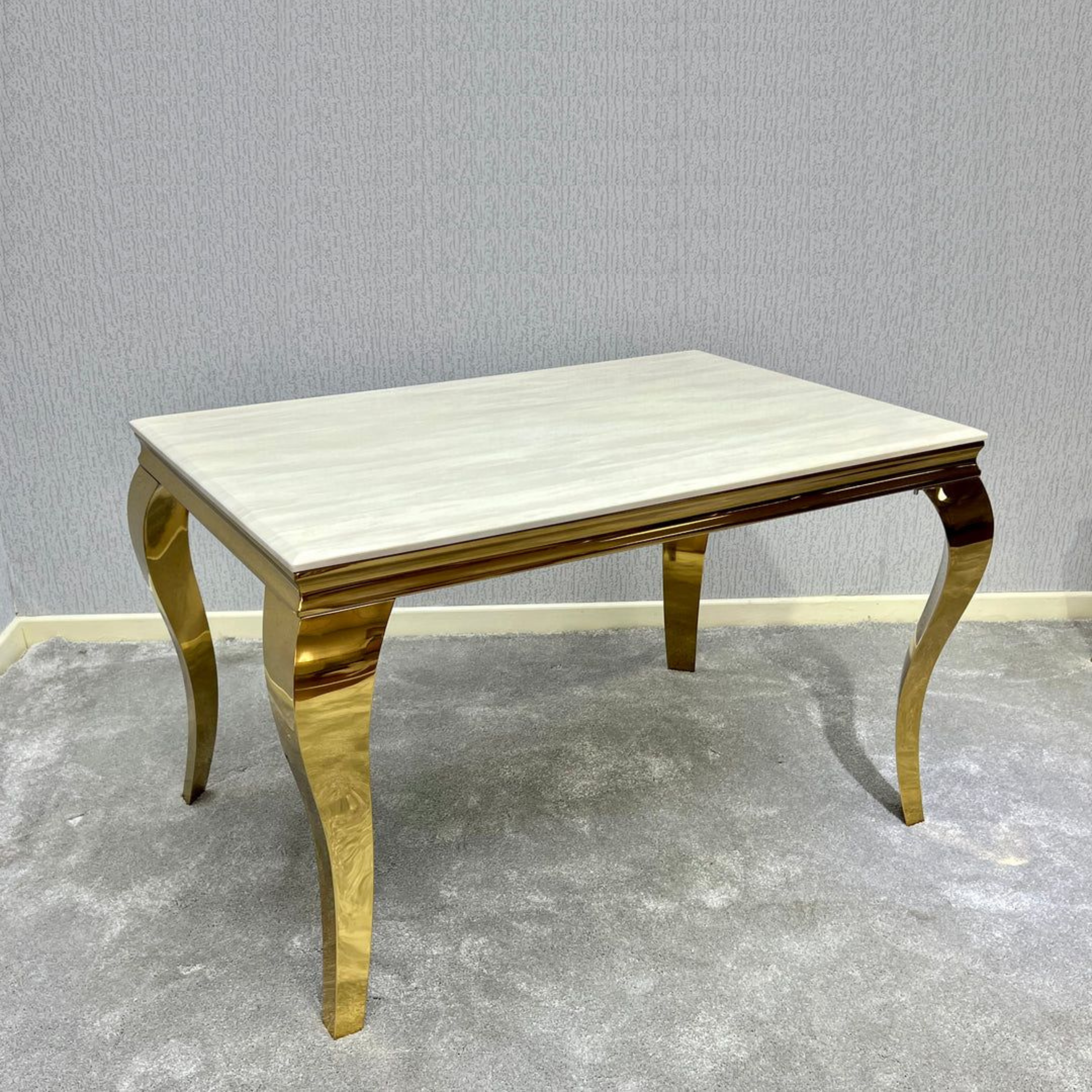 Rectangular table with marble top and gold legs against a gray wall.