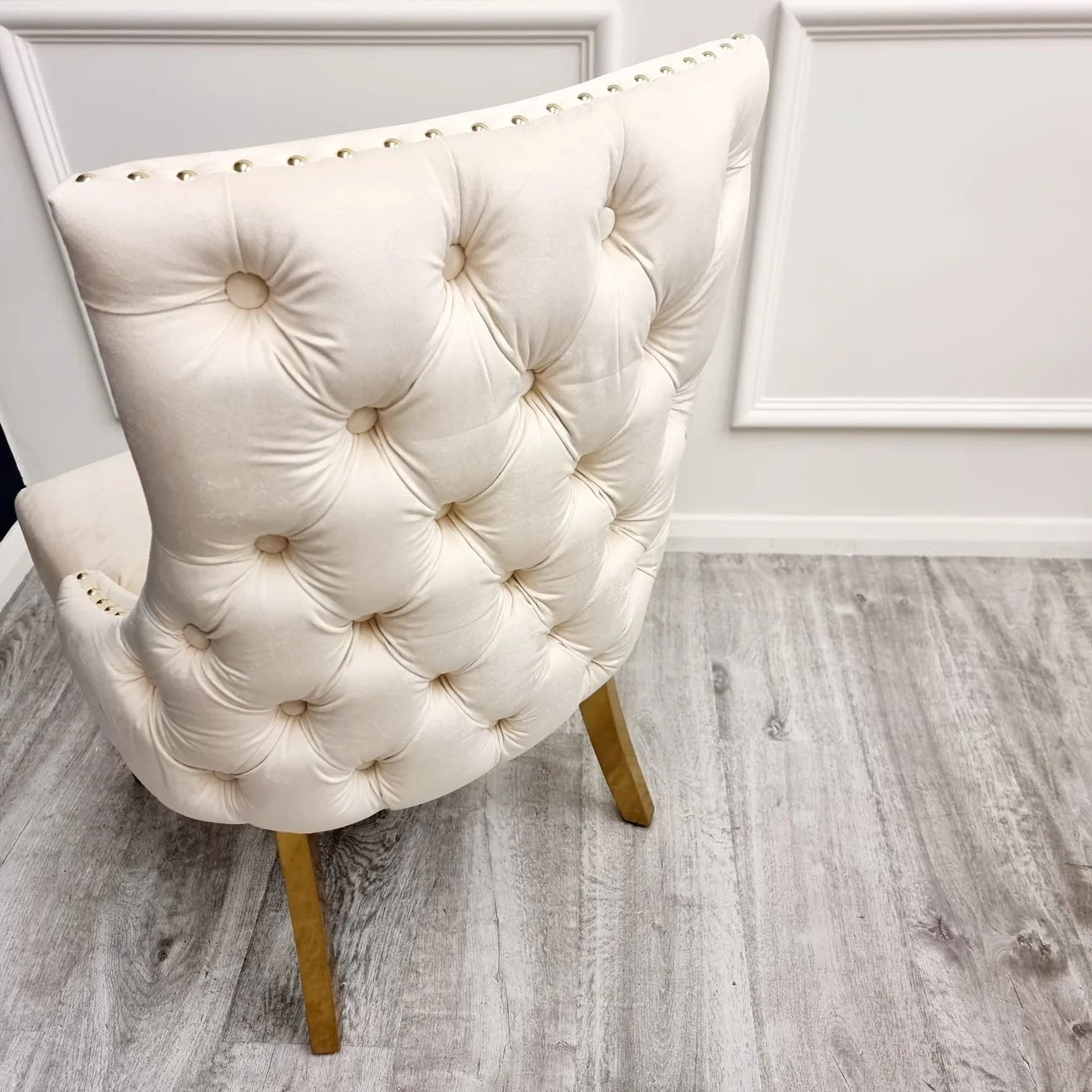 Beige tufted chair on a wooden floor with white walls